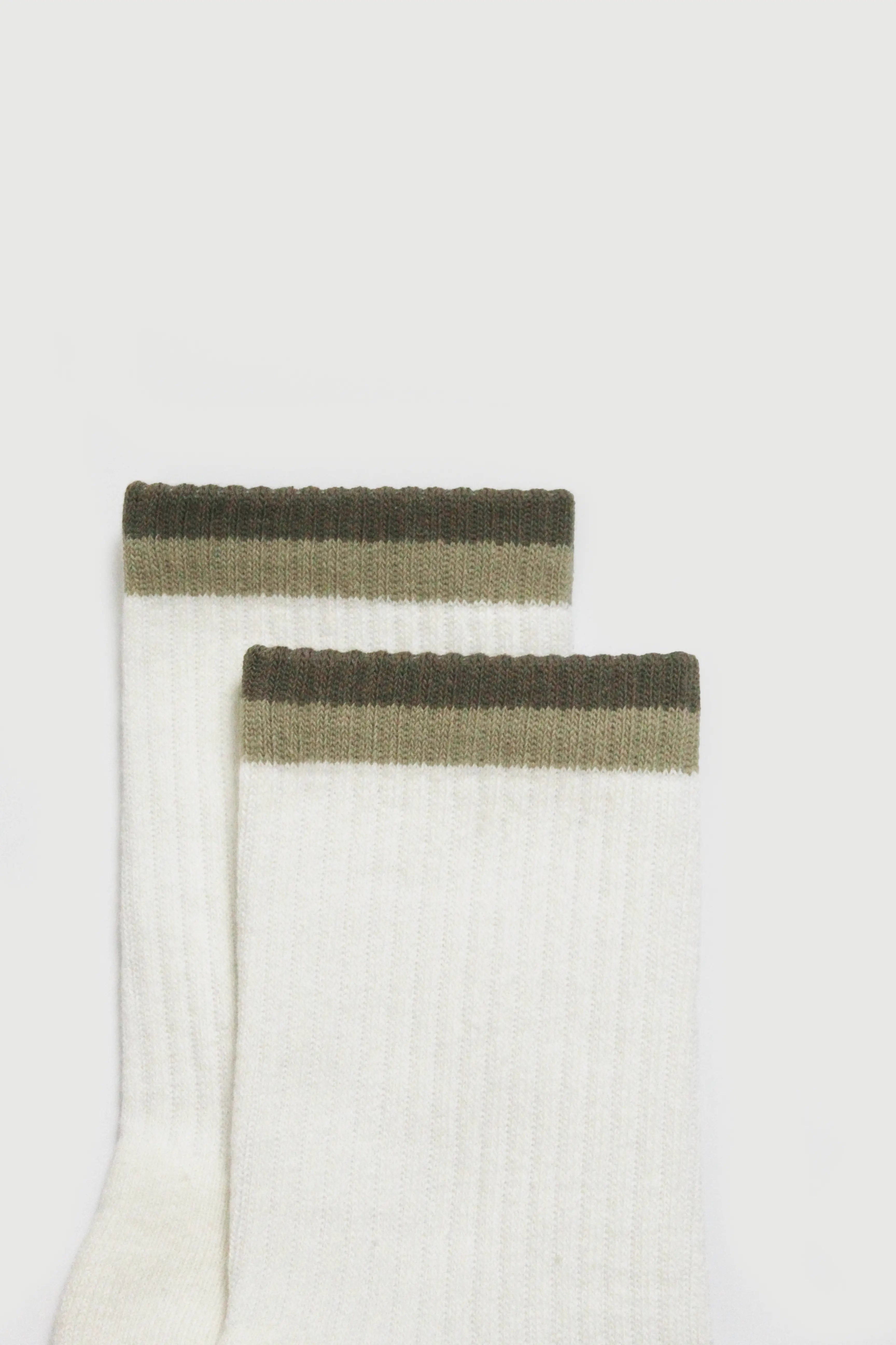 White pilates grip socks with green ribbed cuffs on a light gray background