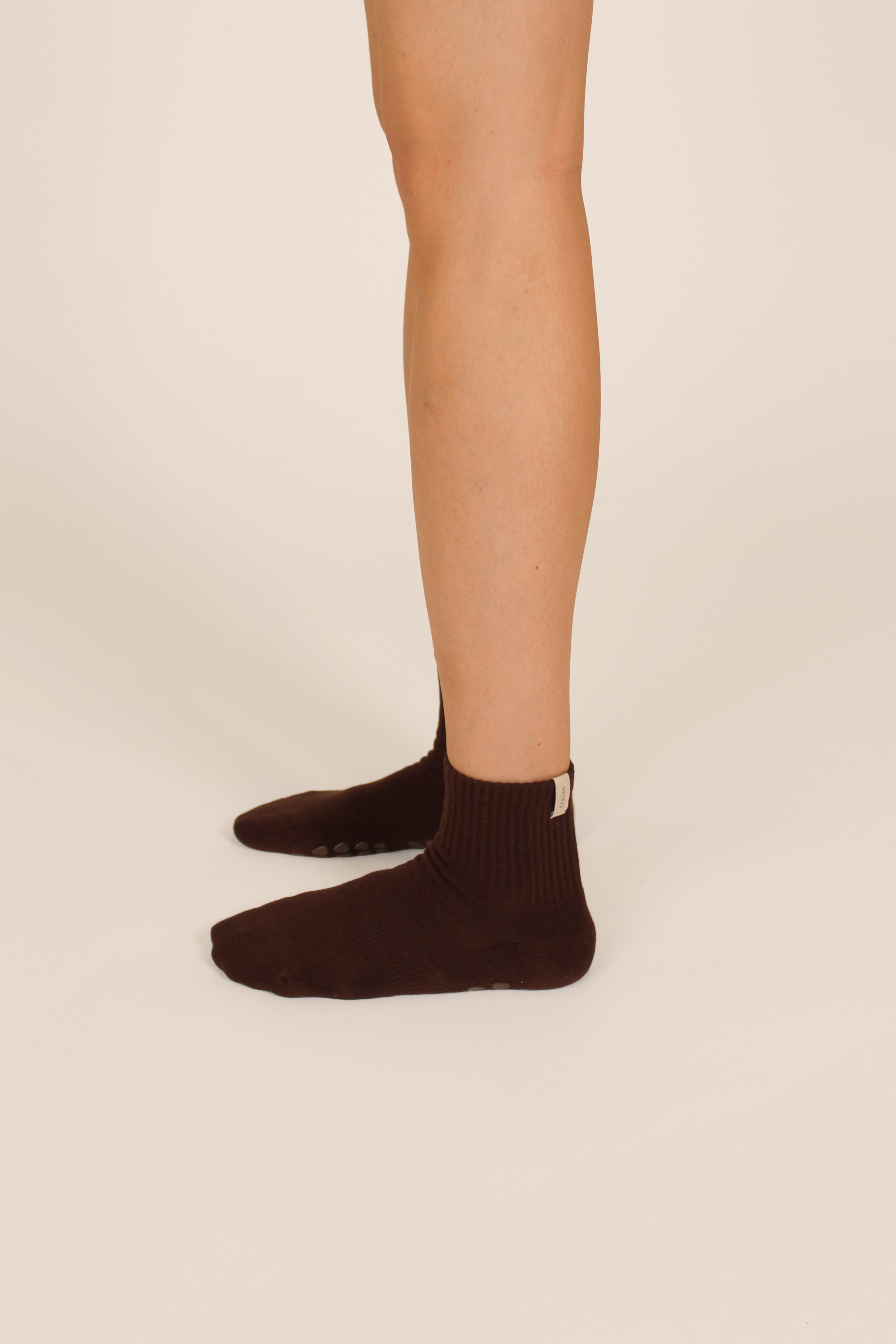 Person wearing espresso brown pilates grip socks on a beige background