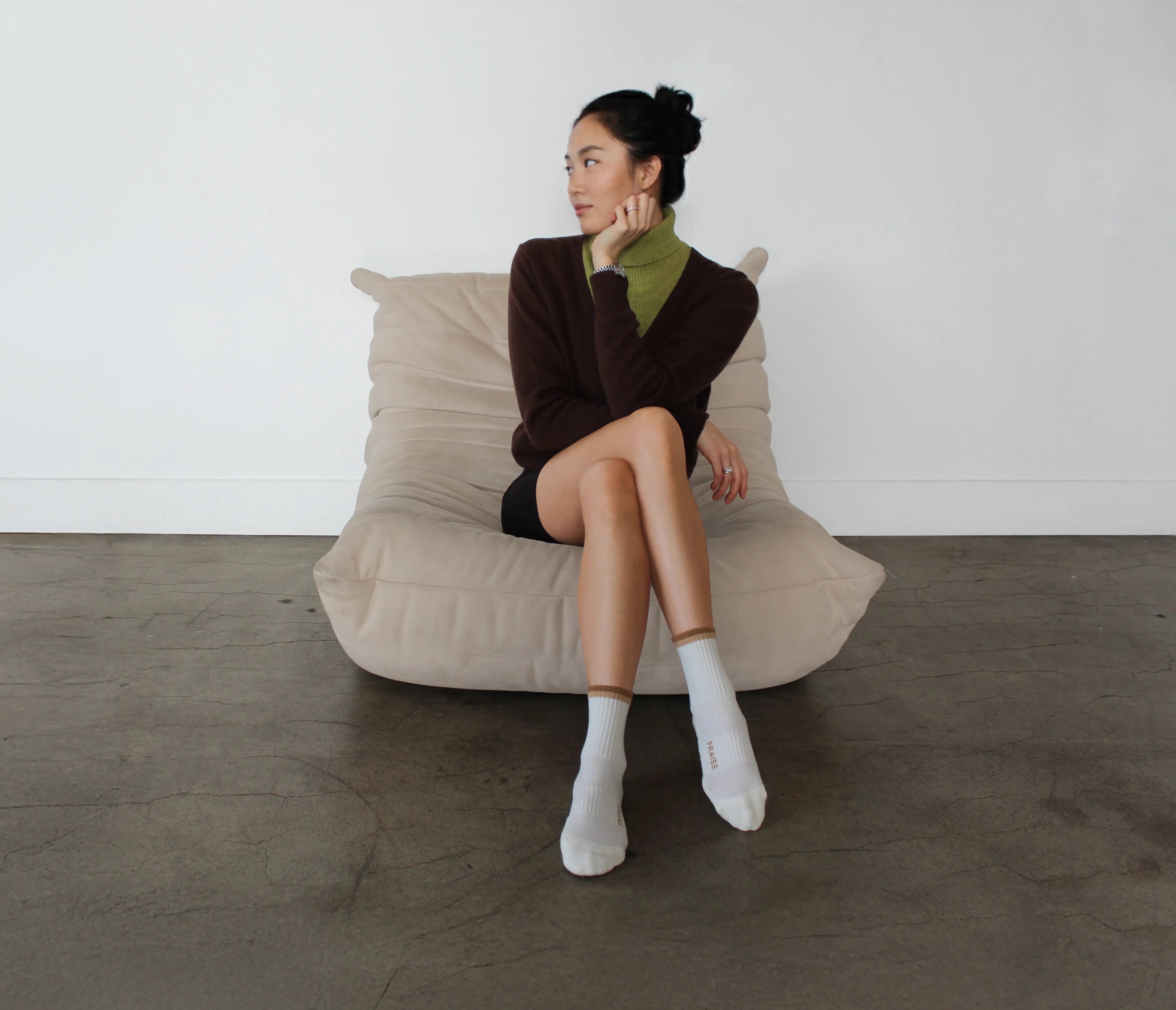 Woman sitting on a beige bean bag chair wearing a brown sweater and white crew grip socks for pilates