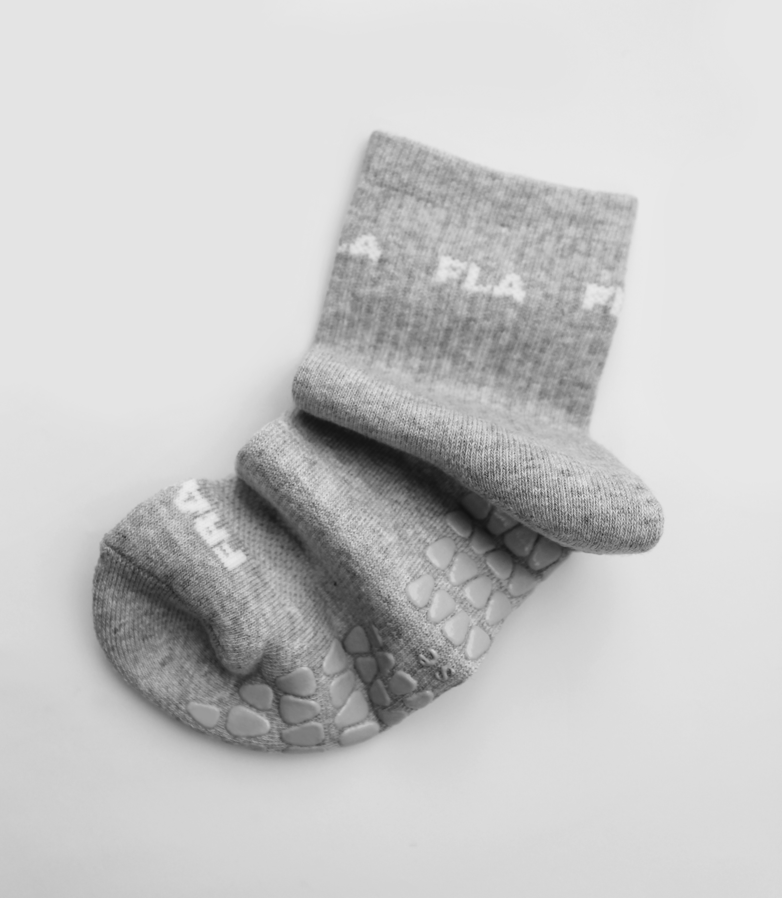 A grip sock from the brand Fraise in a neutral grey color. The sock is scrunched up in an artistic way on a plain background.