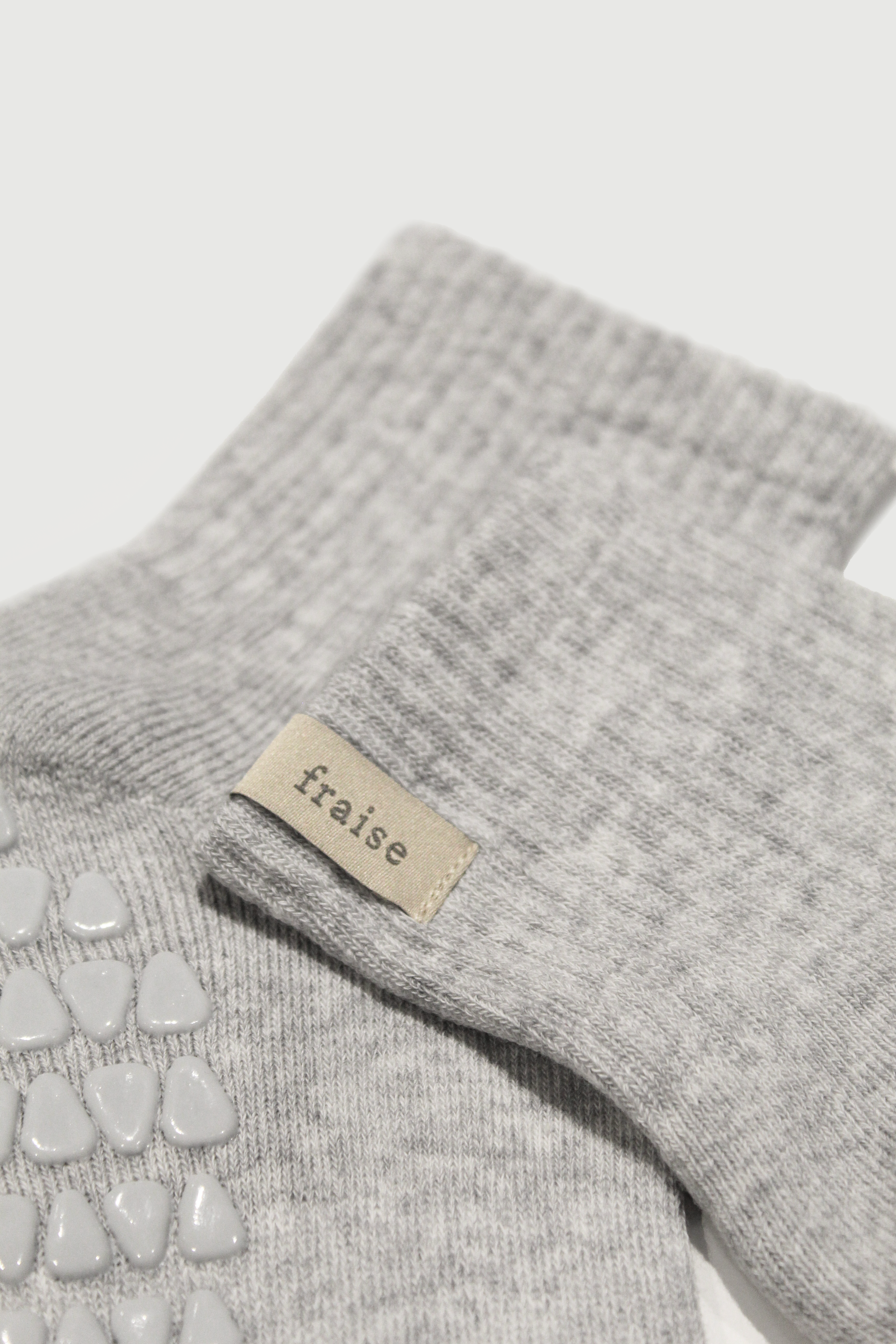 Close up of heather grey quarter length grip socks with a 'fraise' label on a light gray background