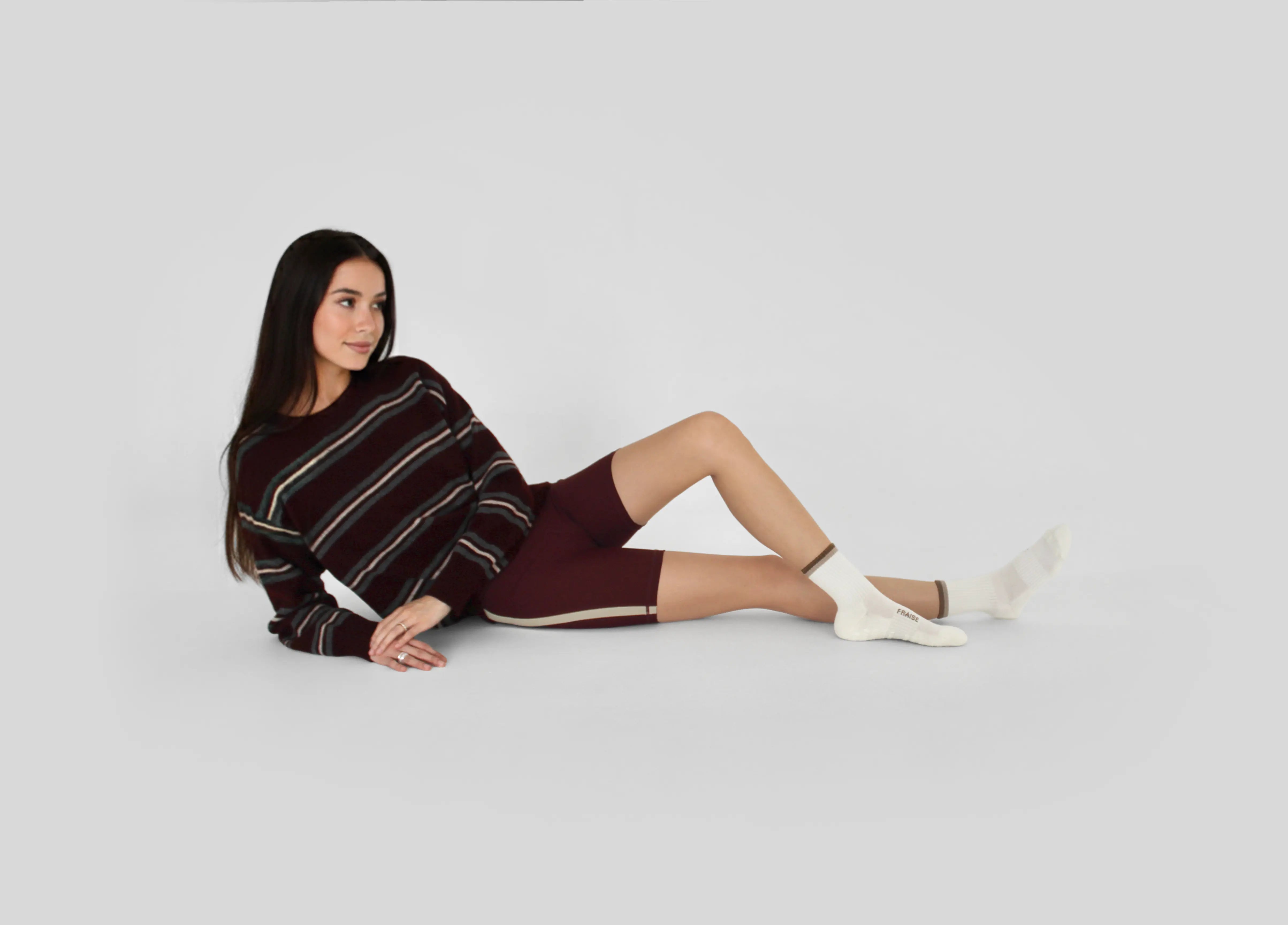 Woman sitting on a white floor wearing a striped sweater and malt striped crew grip socks