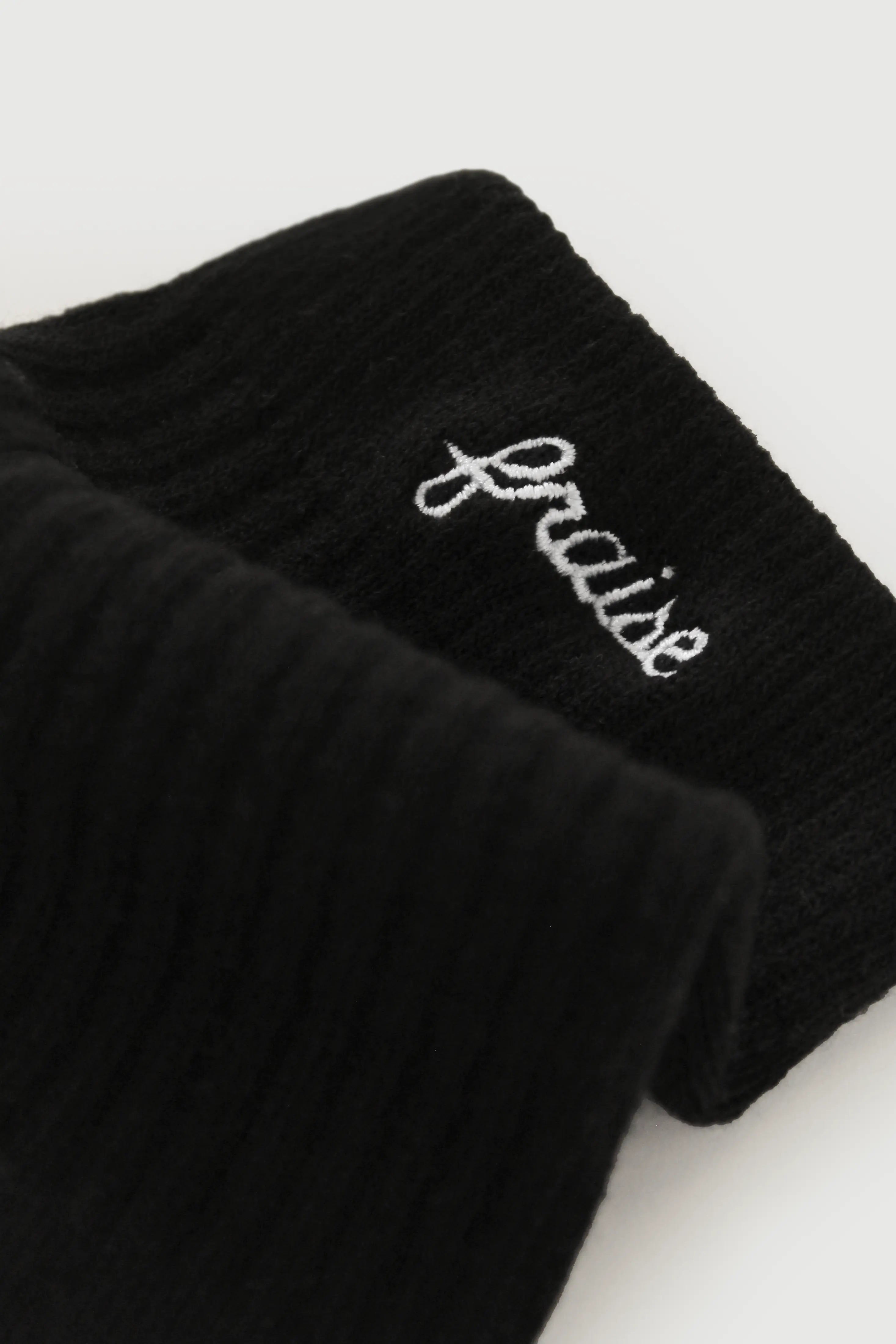 A close-up of a black pilates sock with 'Fraise' embroidered in white script on the side, photographed against a light neutral background.