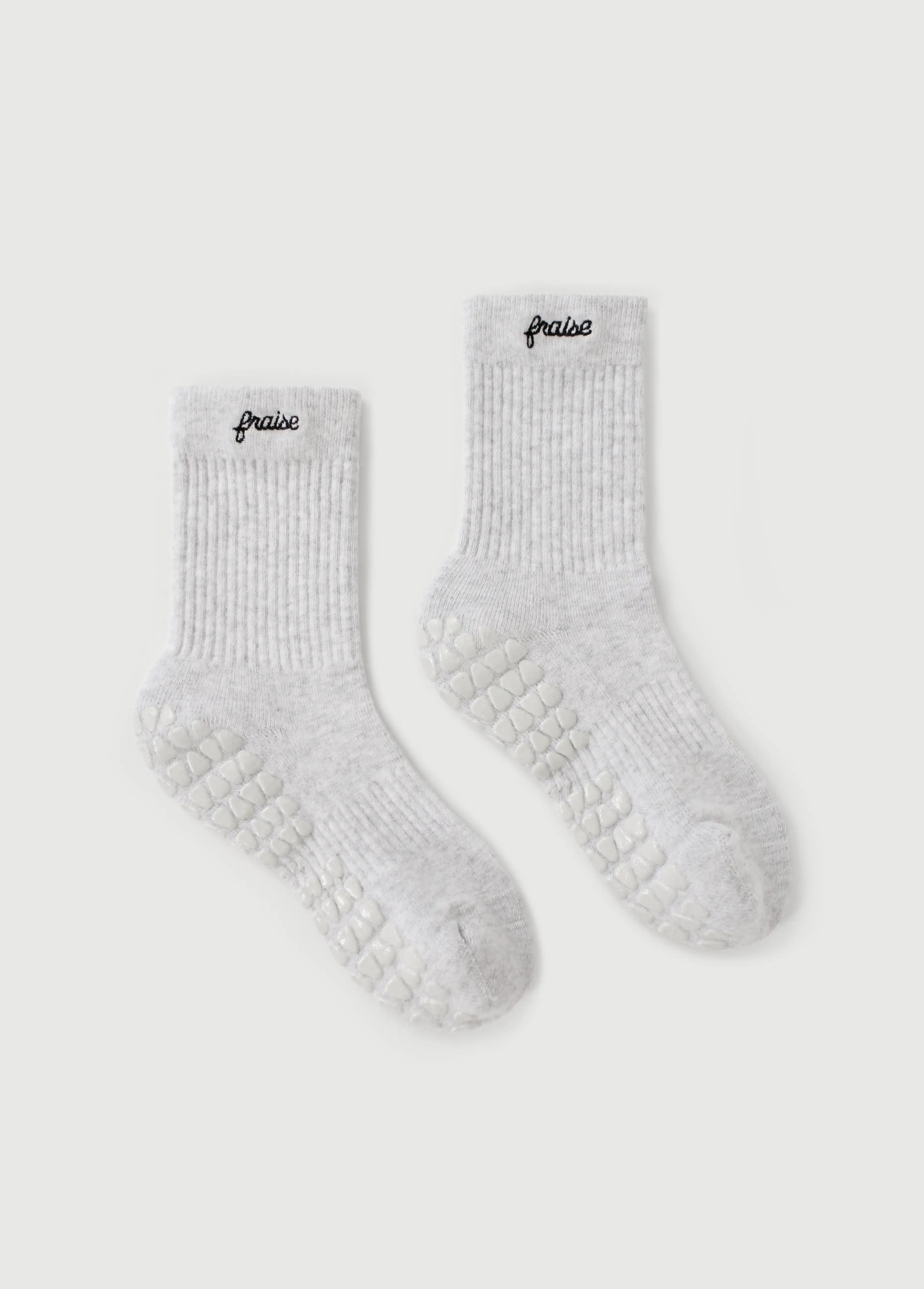 A pair of light gray ribbed socks with textured grip soles for yoga and pilates along with the brand name 'fraise' embroidered in black on the cuff, displayed on a light gray background.