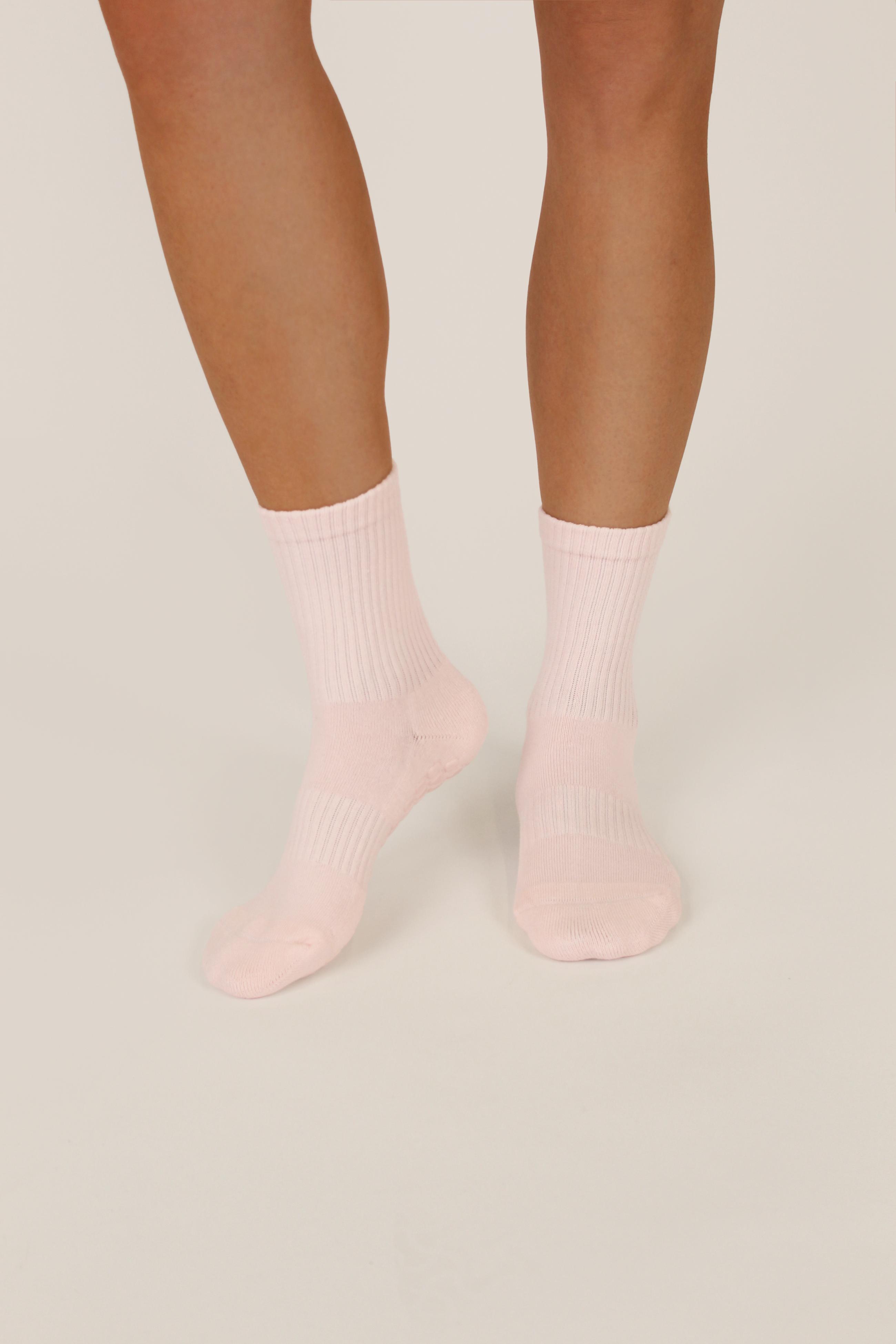 A pair of light pink ribbed crew socks worn on a model's feet, shown against a plain light beige studio background.