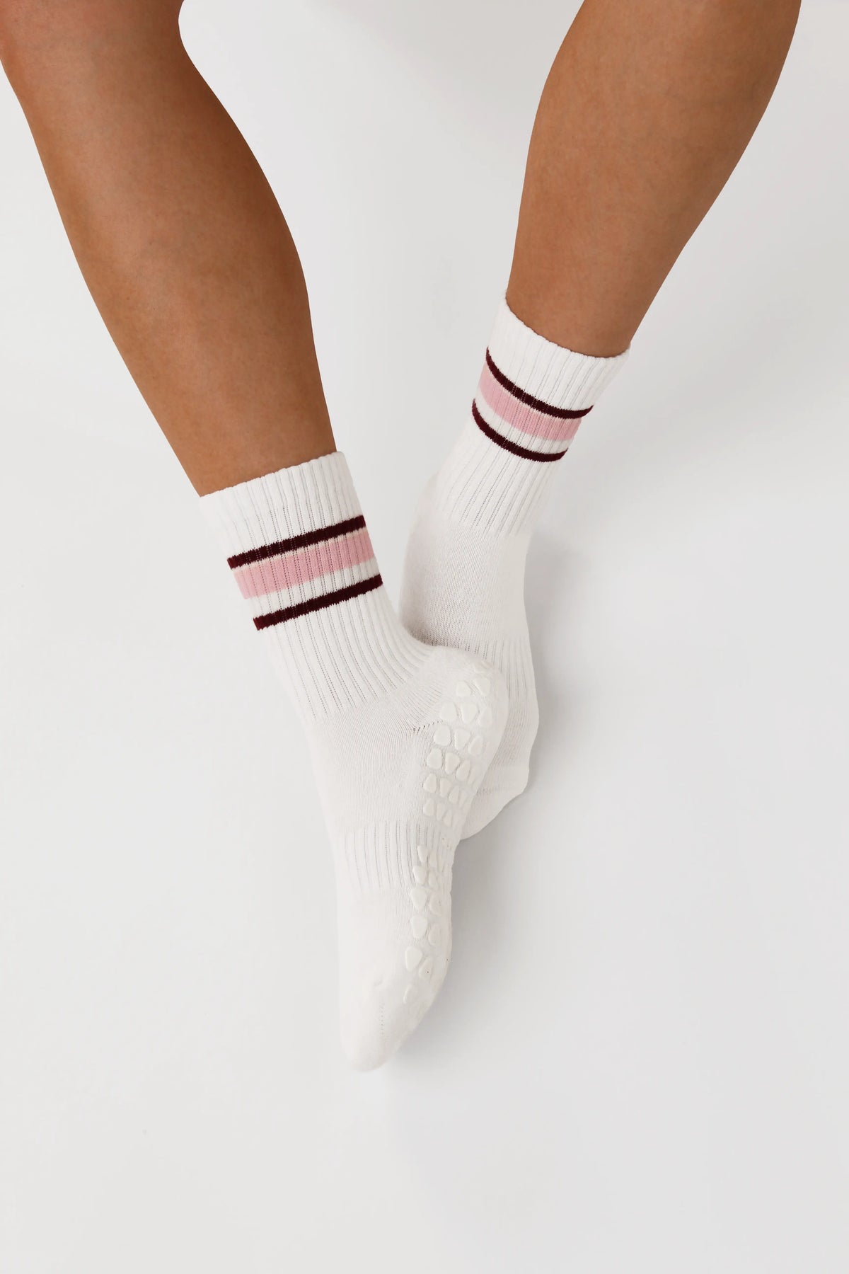 White striped grip socks with pink and dark brown stripes near the cuff, shown worn on a person's feet against a light gray studio background.