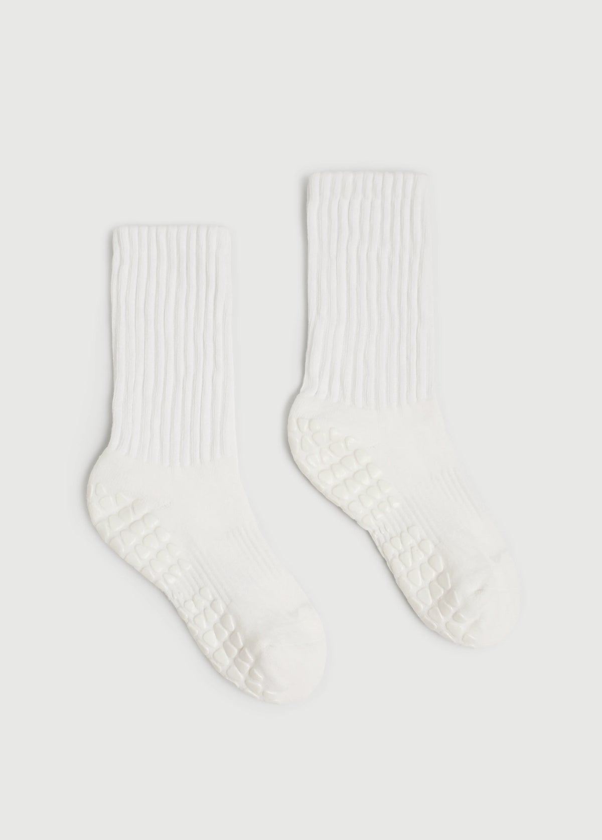 A pair of white ribbed crew yoga socks with textured grip soles, displayed on a light gray background.