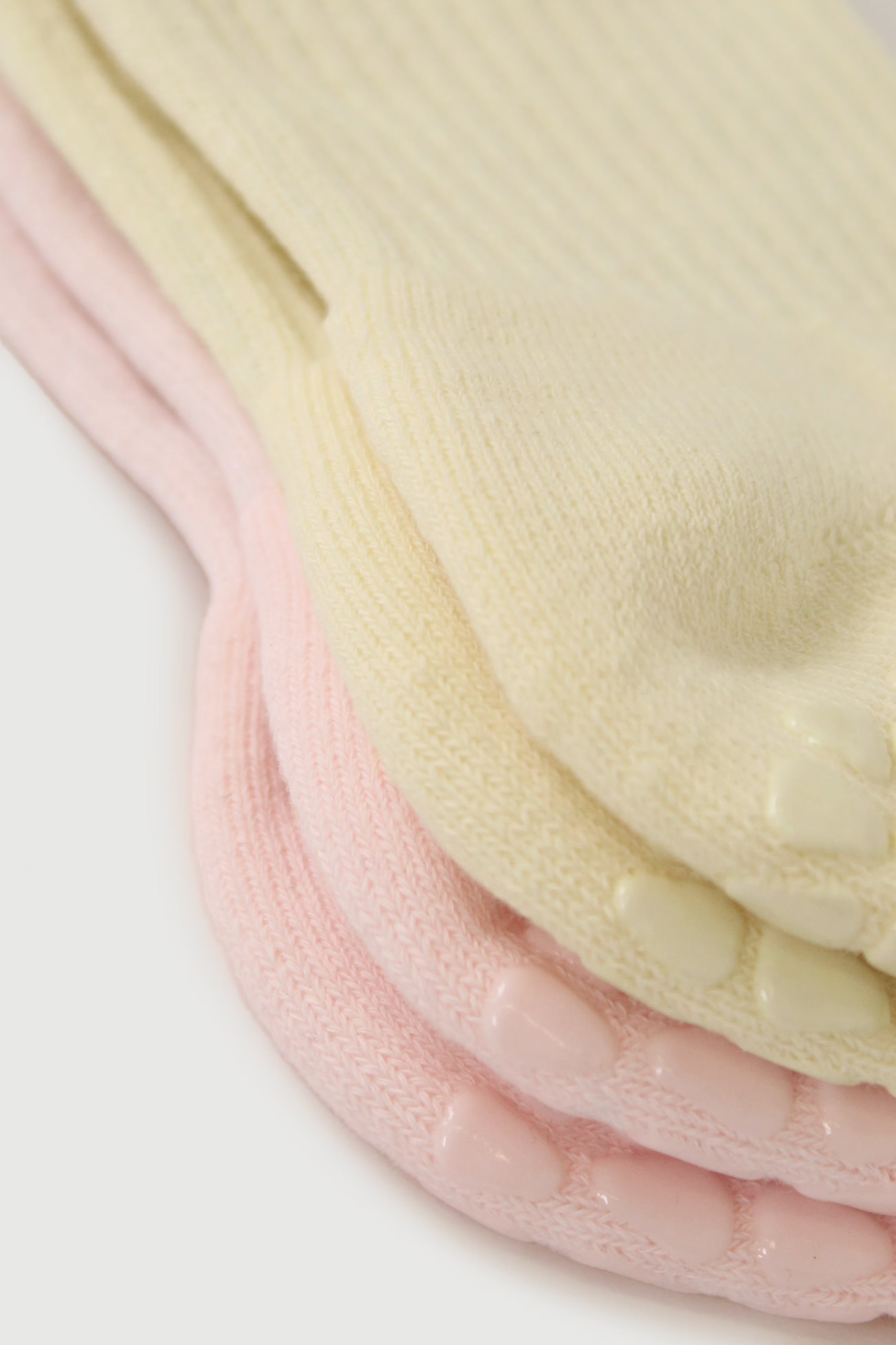 A close-up of a stack of ribbed Fraise grip socks in pale cream and light pink, each with a small raised non-slip grip on the toe area, photographed on a white background.