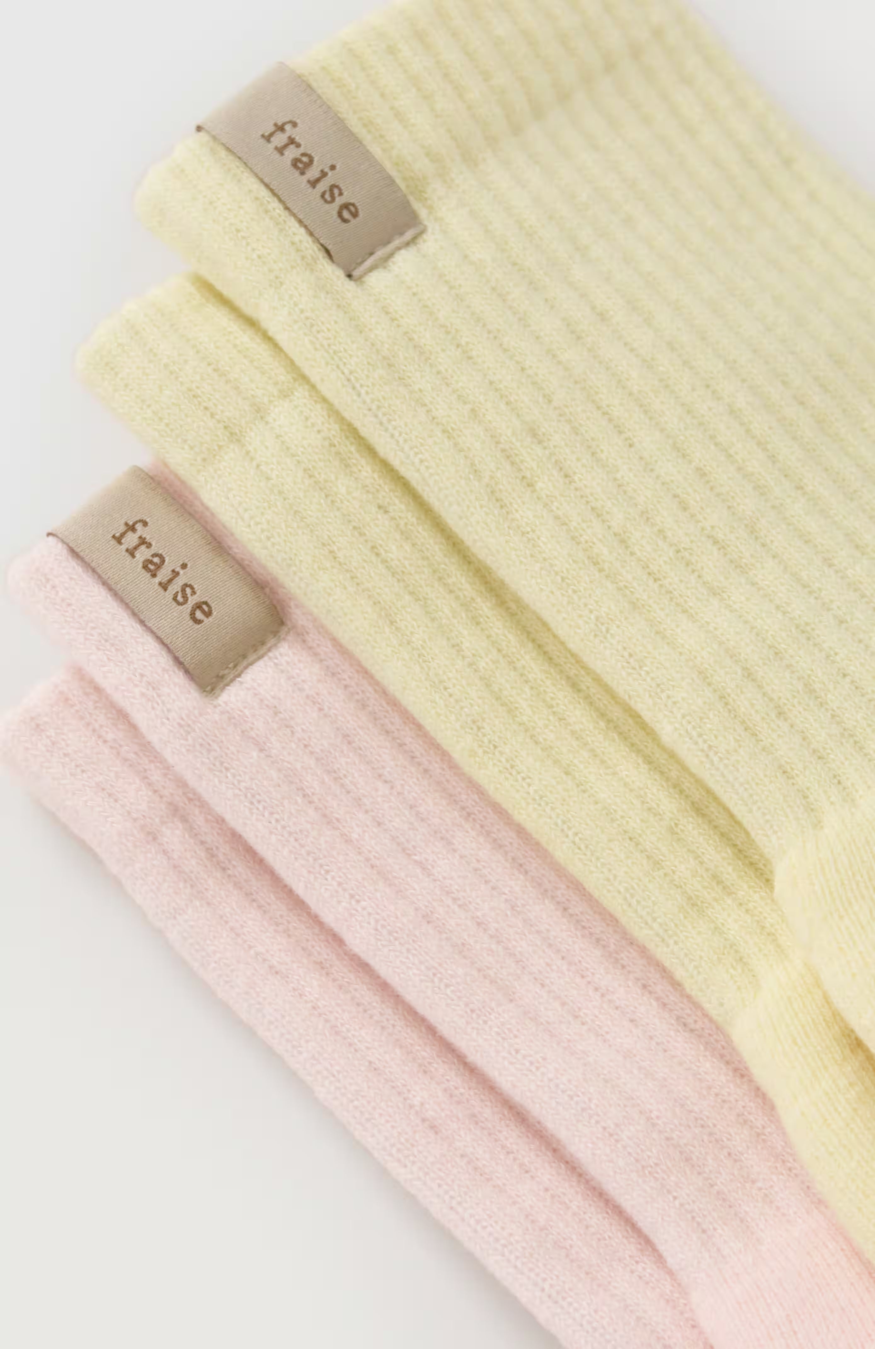 Two pilates reformer grip socks in pale yellow and light pink, stacked diagonally with a small beige brand fabric label reading "Fraise" on each.