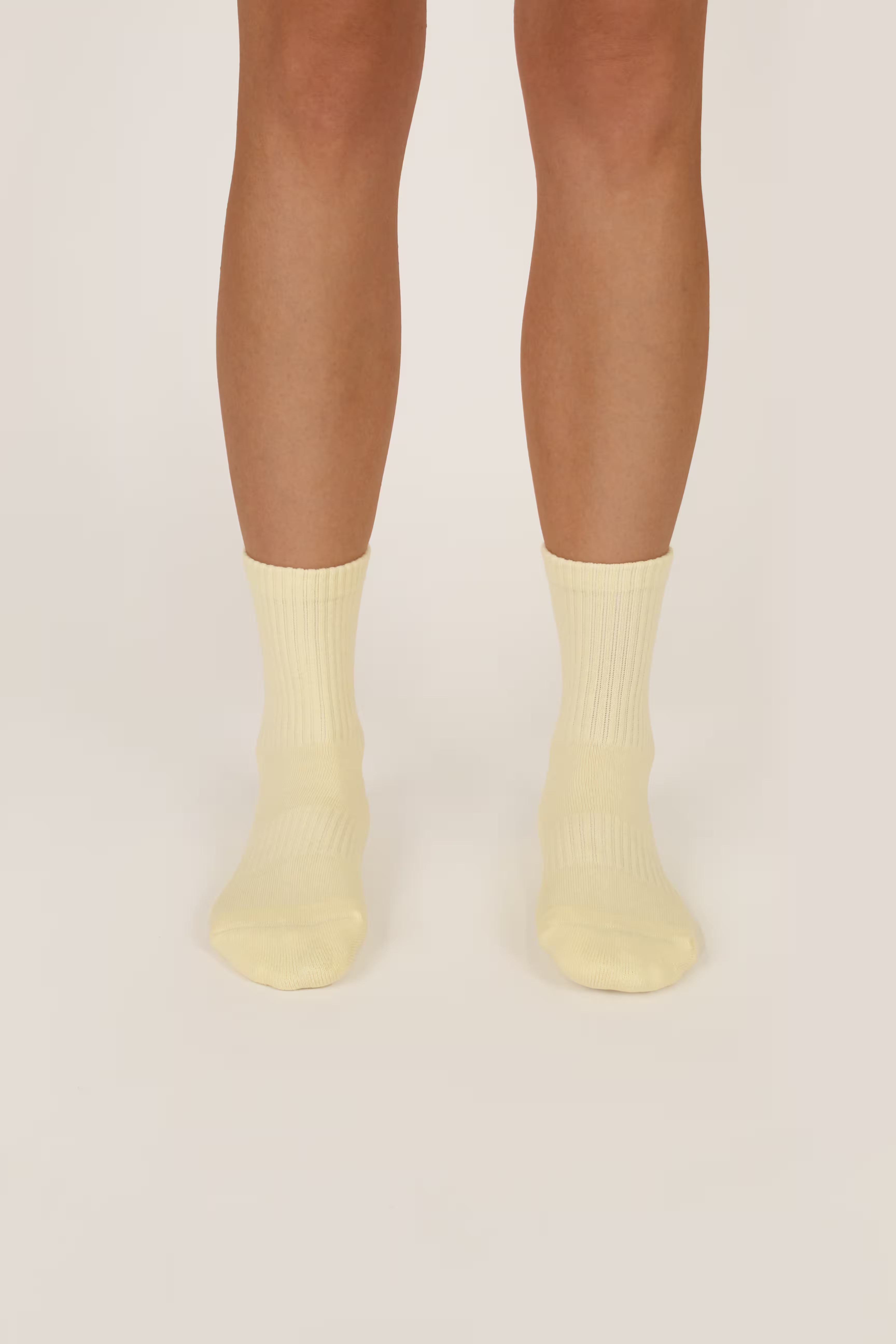 A pair of ribbed pilates crew socks in a pale pastel yellow, worn on a Fraise model's feet against a solid light beige background.
