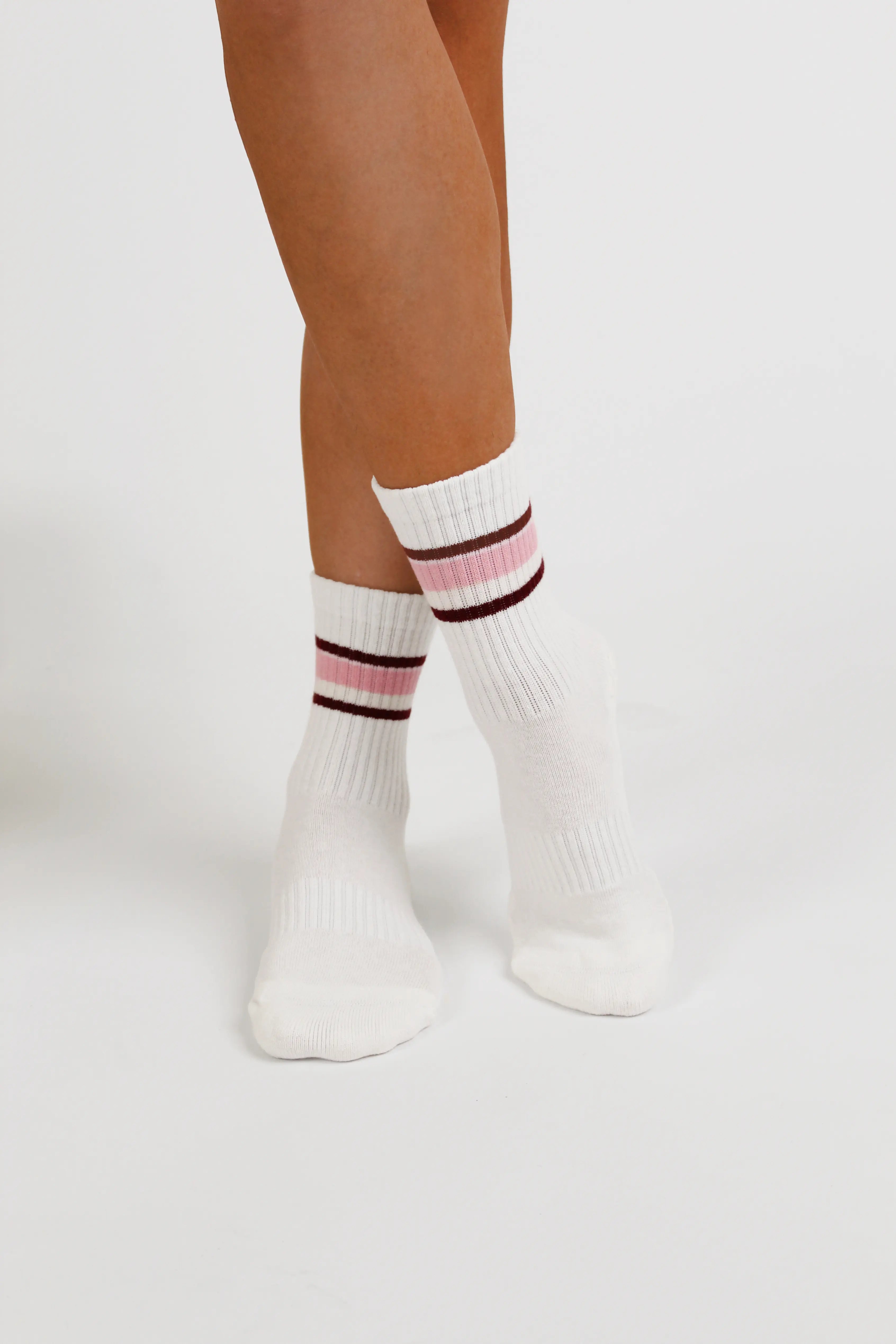 White ribbed Fraise yoga socks with pink and dark red stripes near the cuff, shown on a model's feet against a light gray studio background.