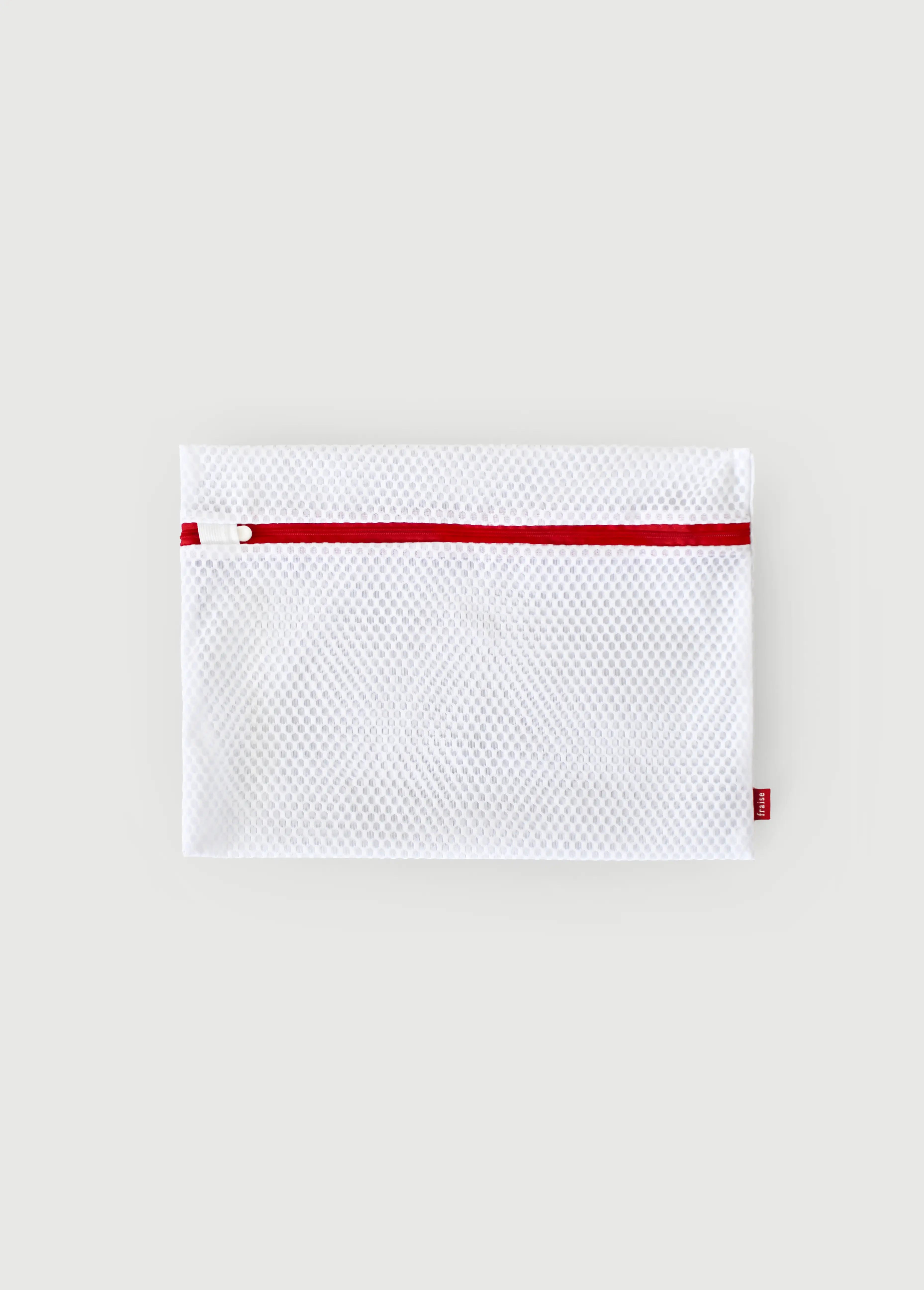 A white mesh zippered laundry bag pouch with a red zipper track and a small red Fraise brand tag, shown flat against a light gray background.