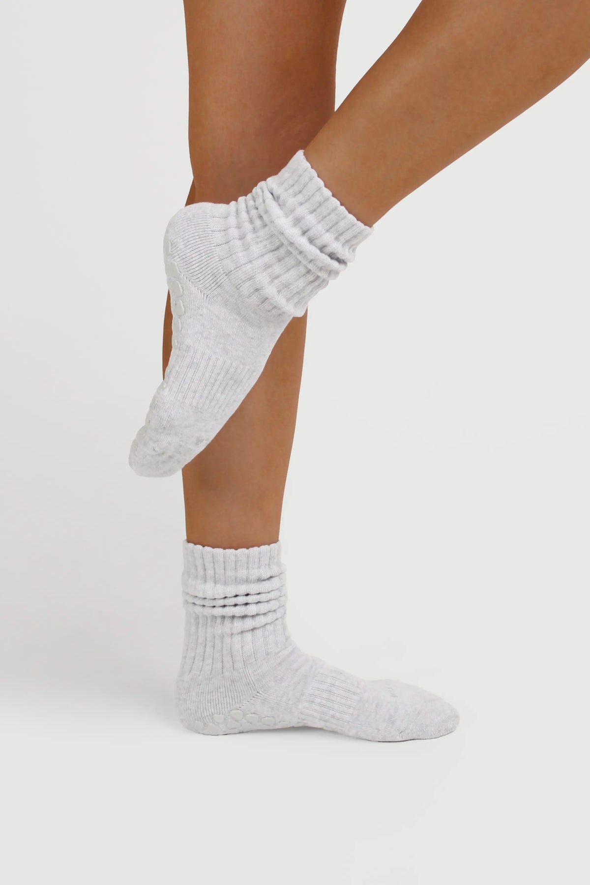 A pair of light gray ribbed slouchy Fraise grip socks worn on a person's feet, shown against a clean light gray studio background.