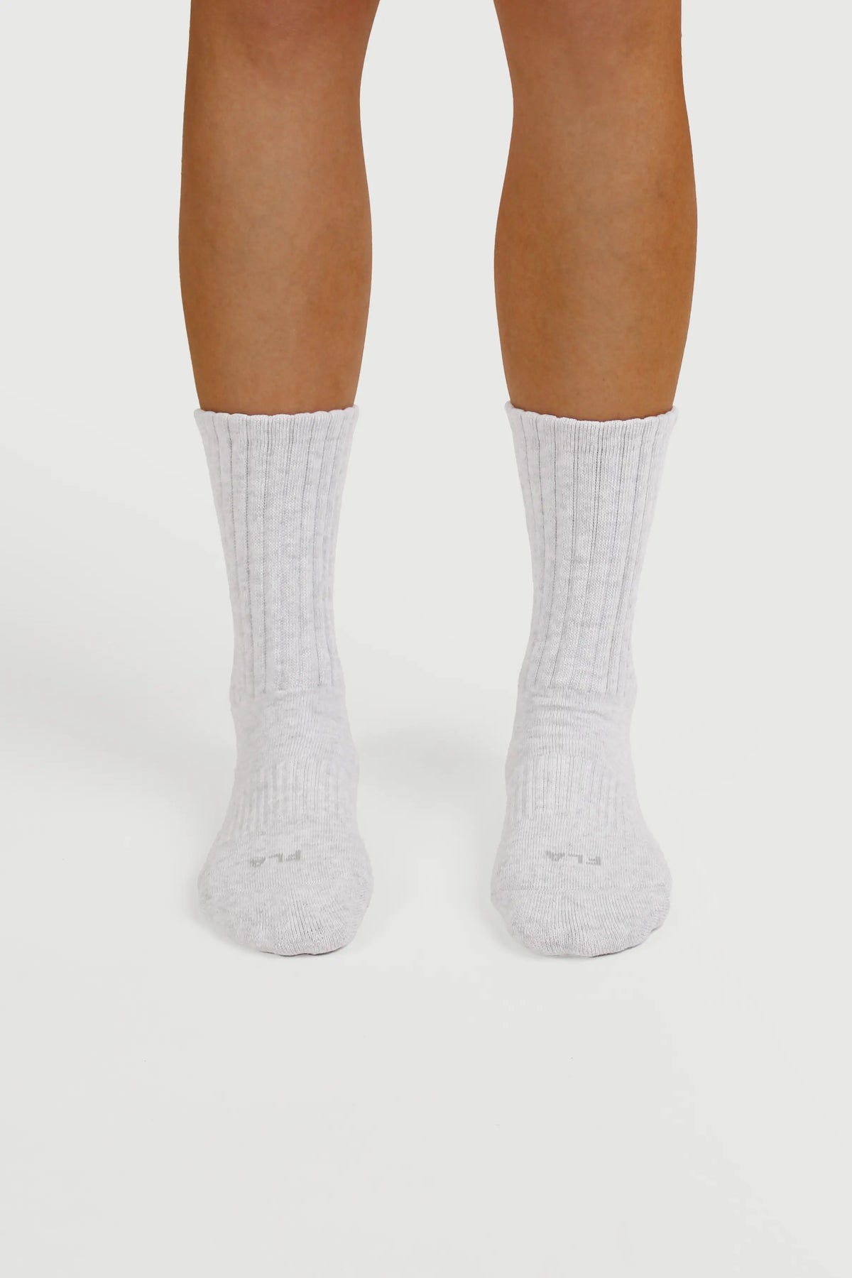 A pair of light gray grip socks worn on a person's feet, shown from the toes to the calves against a clean white studio background.
