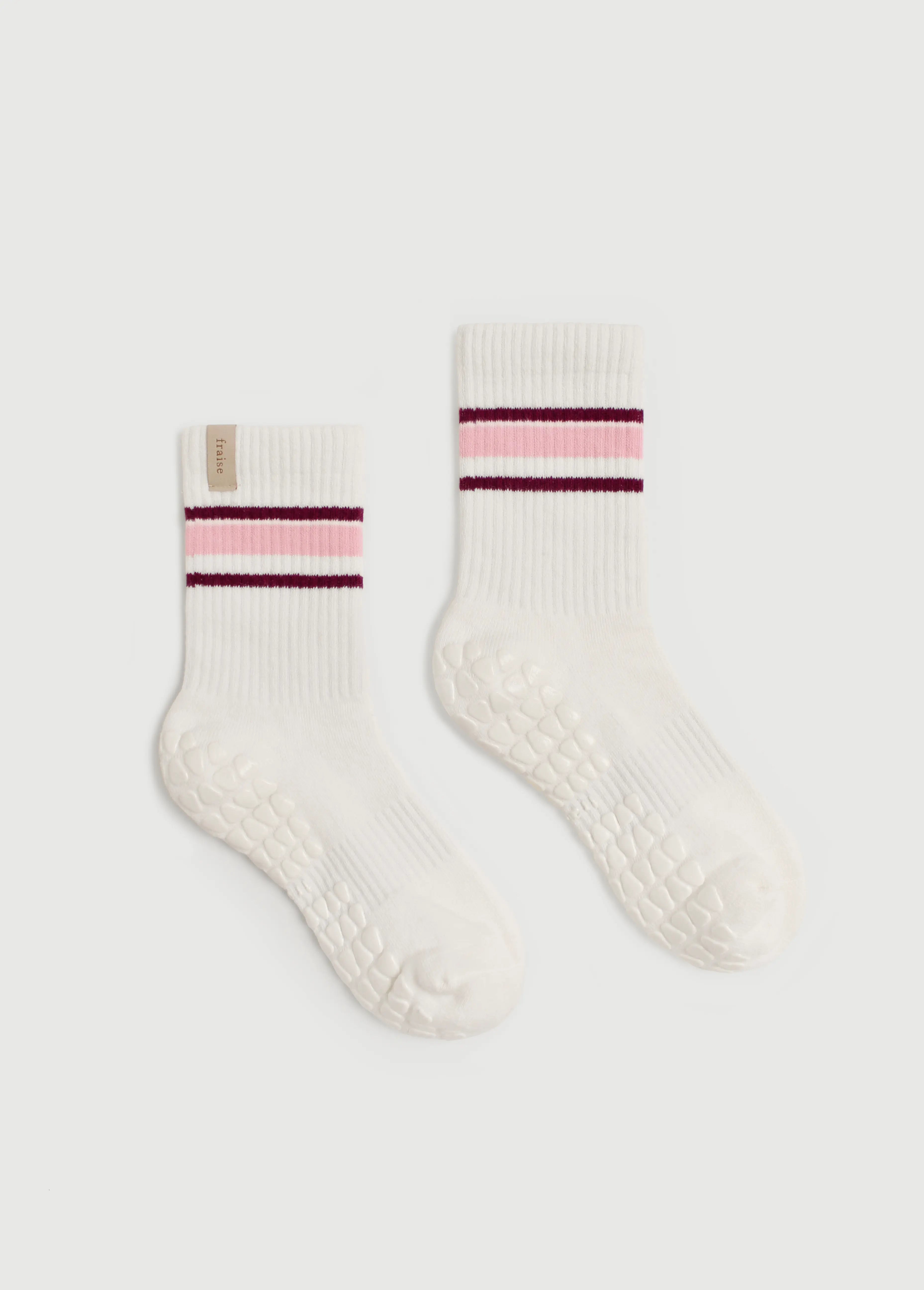 A pair of off-white ribbed Fraise grip socks for pilates reformer with textured grip soles, featuring a striped cuff with pink and dark burgundy bands, displayed on a light gray background.