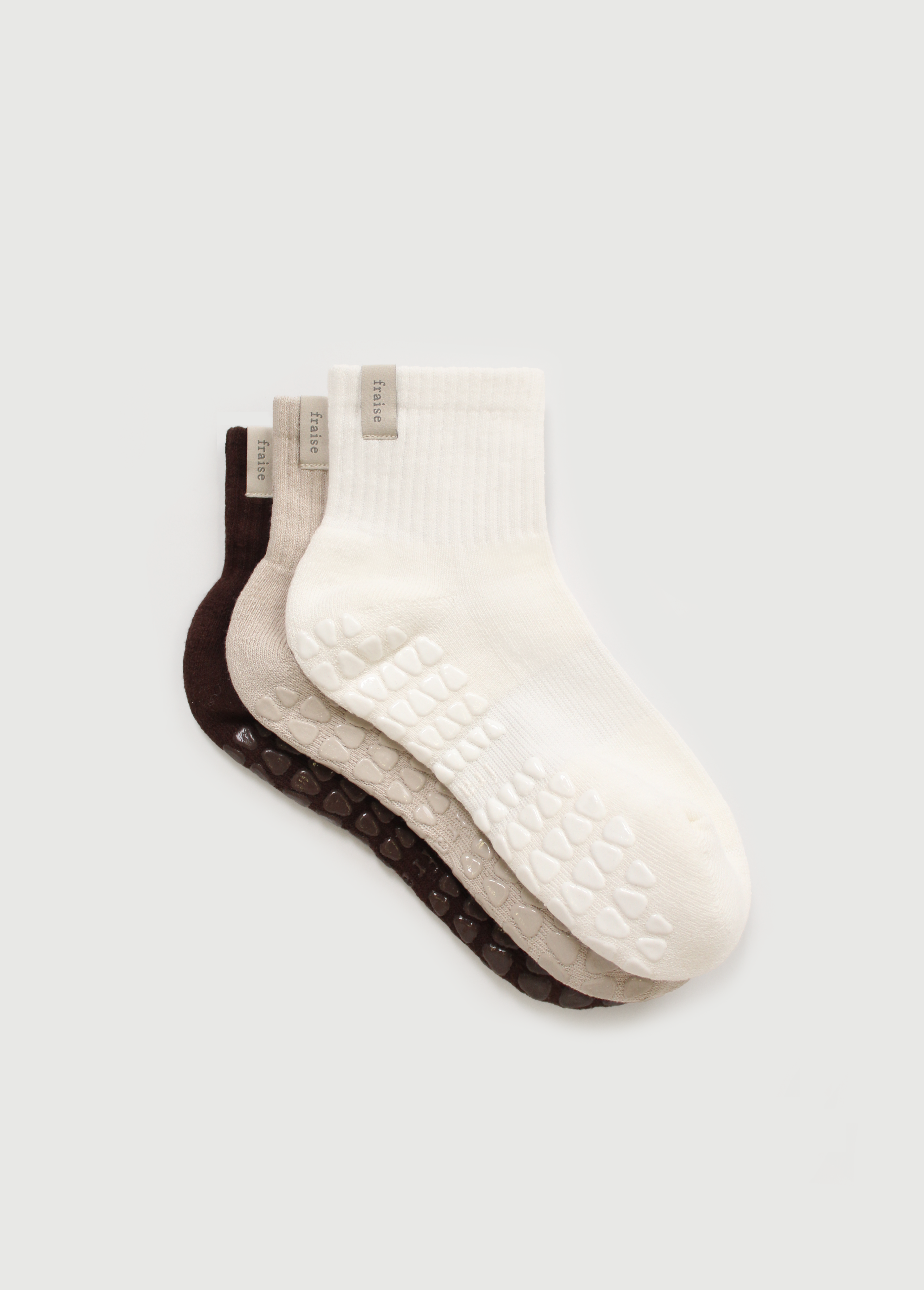 Three pairs of pilates grip socks in brown, tan, and white on a light gray background