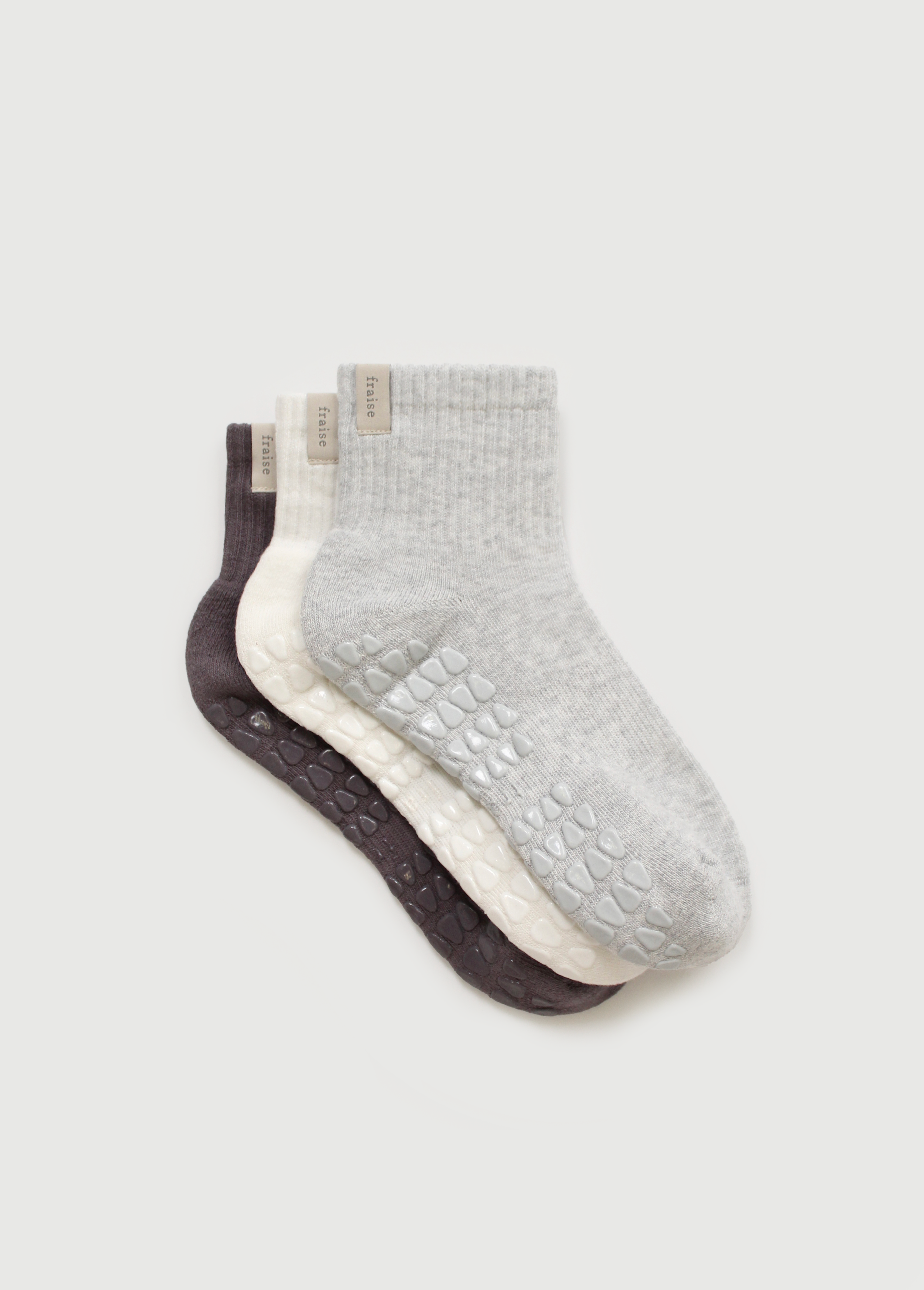 Three pairs of pilates grip socks in gray, white, and black on a light gray background