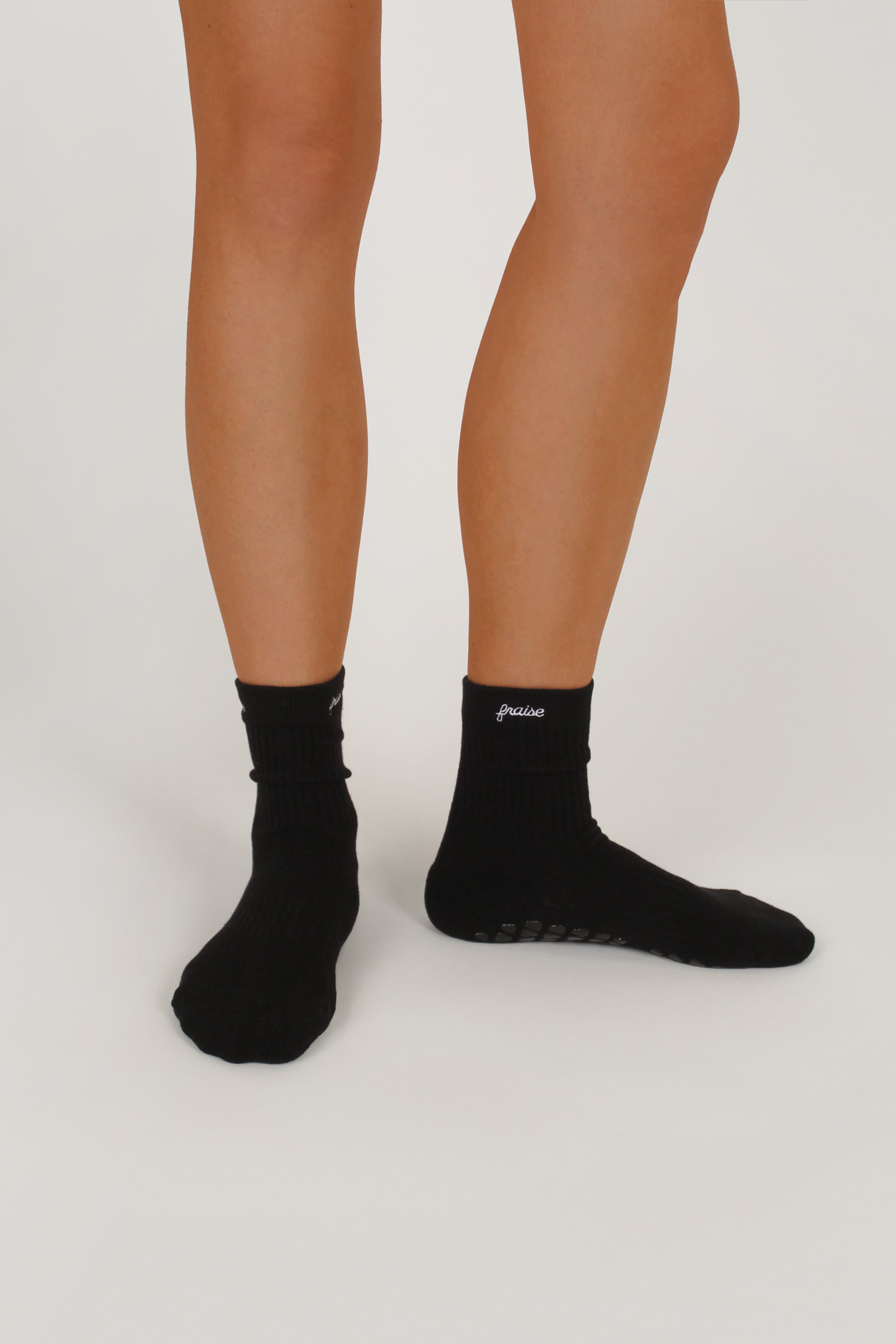 Black athletic crew grip socks worn on a person's feet, shown against a plain light gray studio background. A small white logo, "Fraise" is embroidered on the side of the ankle.